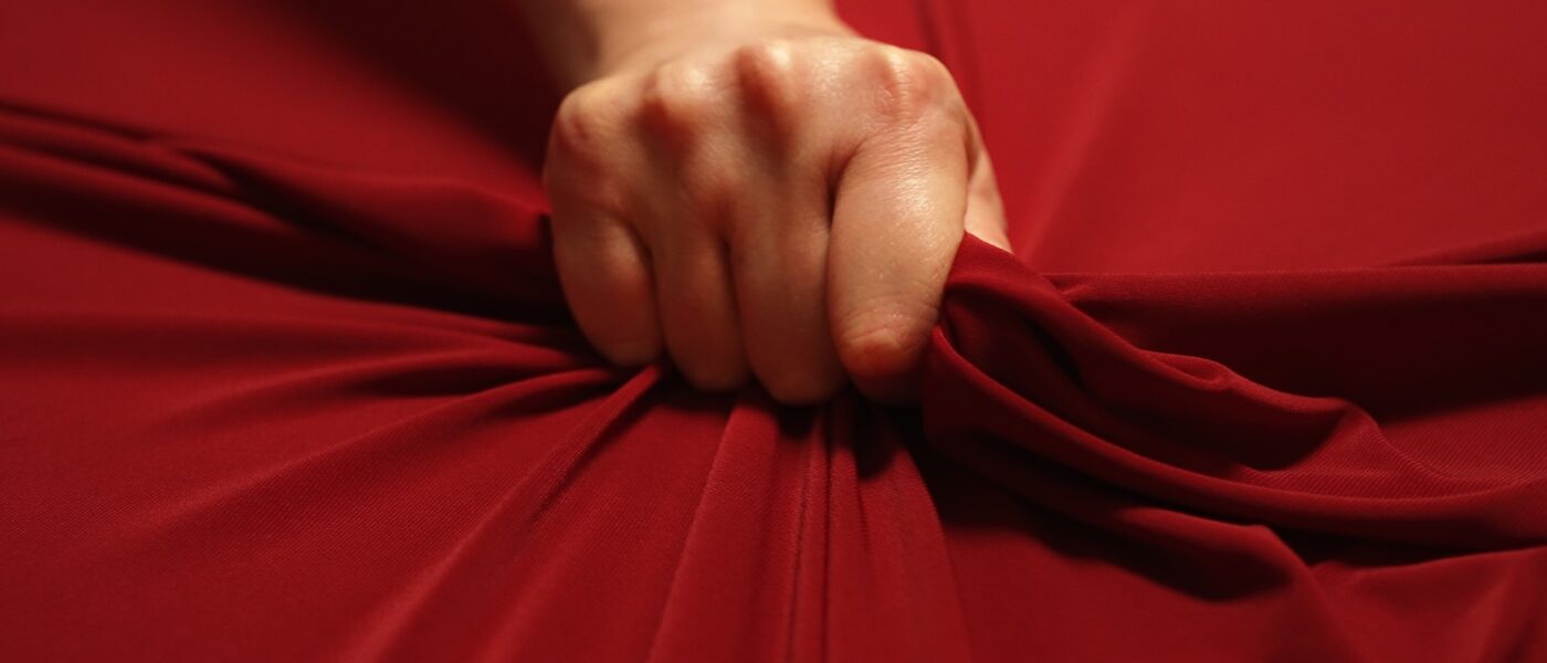 Woman hand passionately squeezes red bed sheet. Love concept.