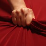 Woman hand passionately squeezes red bed sheet. Love concept.