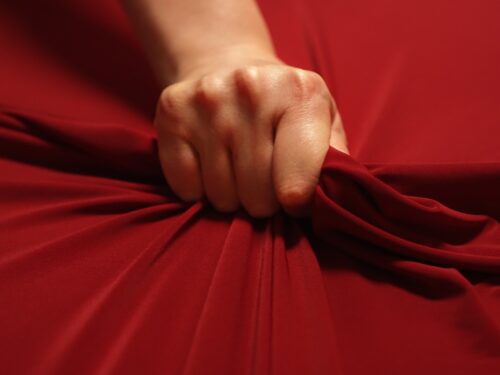 Woman hand passionately squeezes red bed sheet. Love concept.