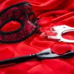 BDSM concept: crop, handcuffs and eyemask on red satin