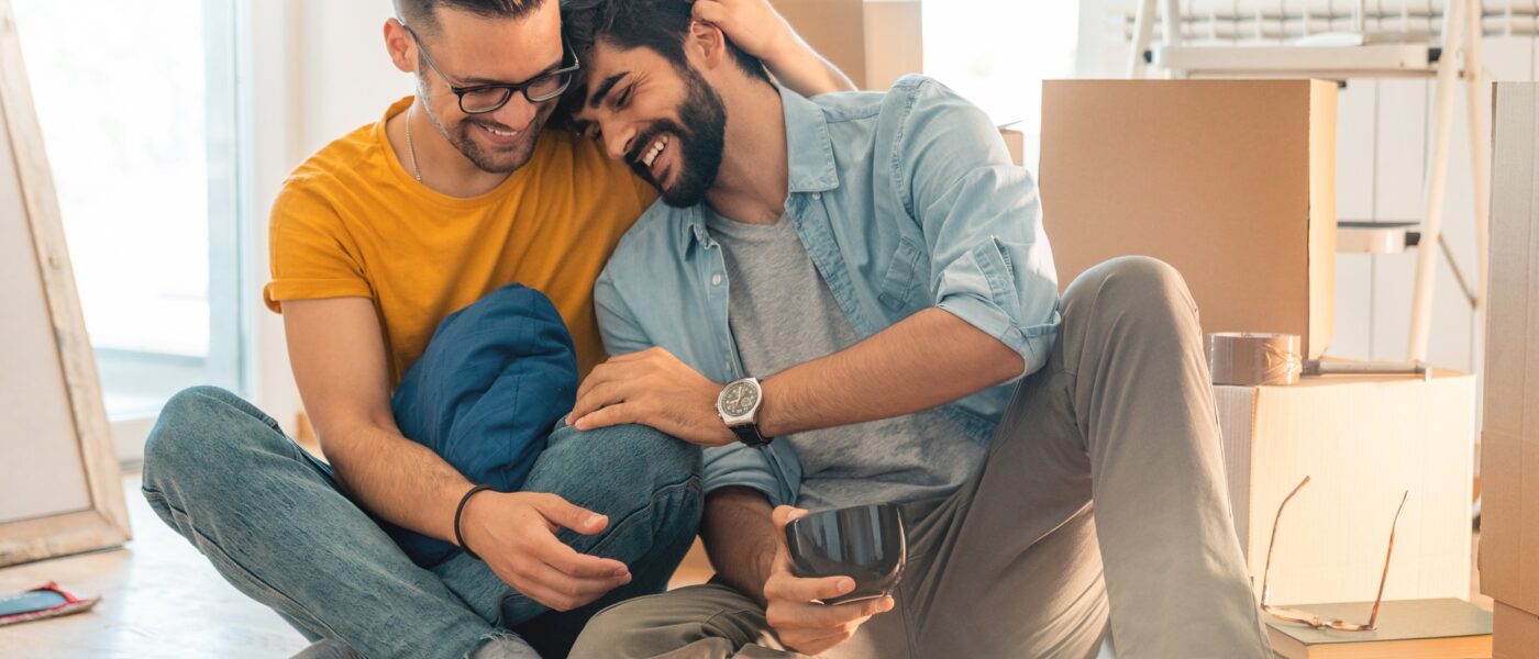 Cute homosexual couple sitting on floor and enjoying new home