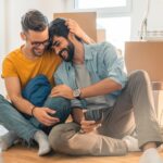 Cute homosexual couple sitting on floor and enjoying new home