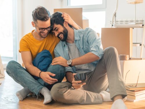 Cute homosexual couple sitting on floor and enjoying new home